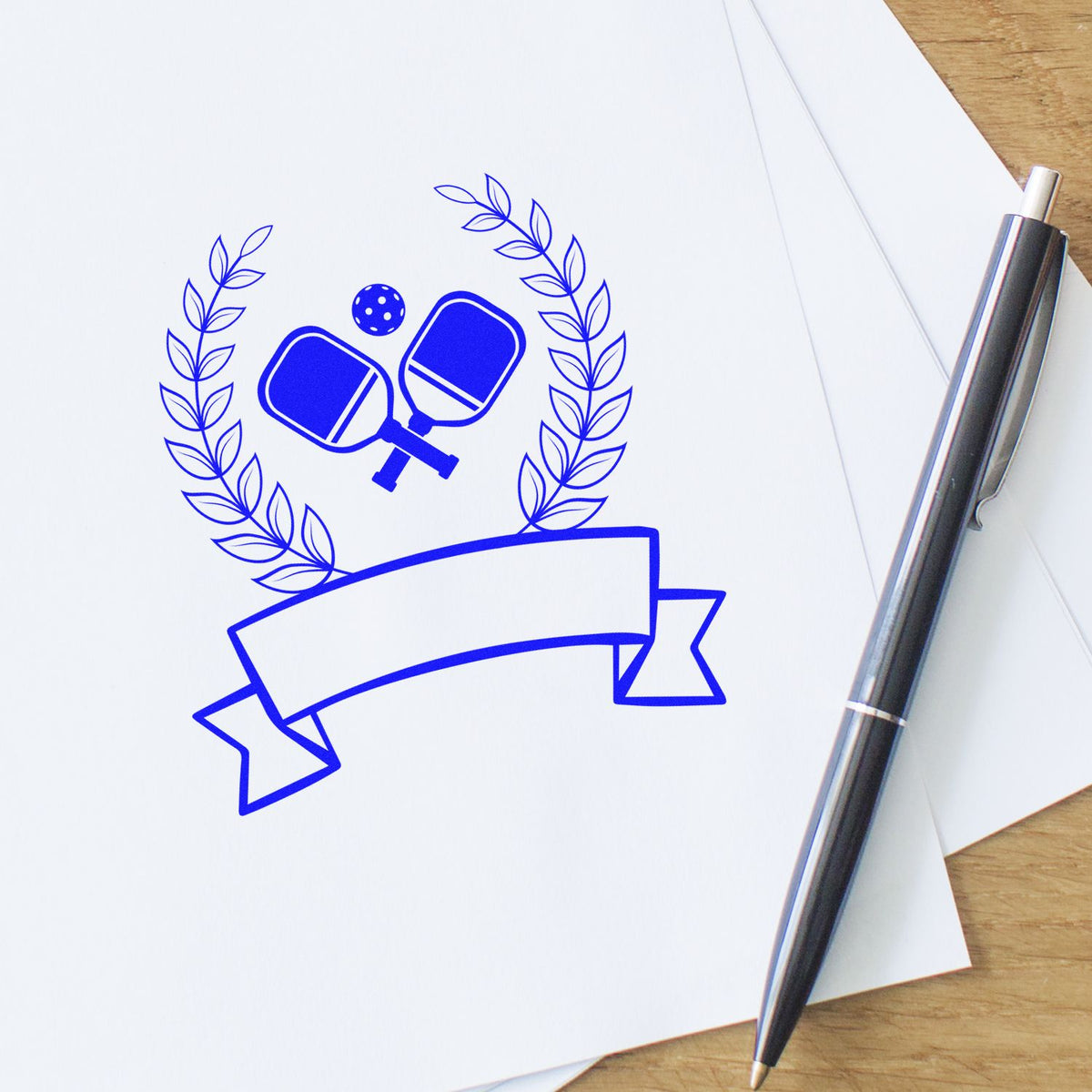 Blue custom stamp and seal with laurel wreath, crossed paddles, and blank ribbon on white paper beside a pen
