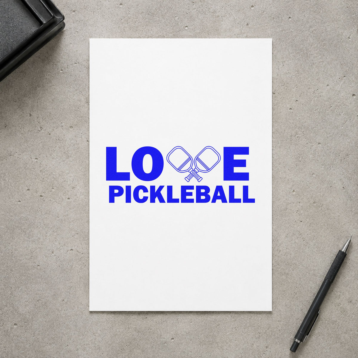 Love Pickleball Crossed Paddles craft stamp imprinted in blue ink on paper, a design suited to framed shop wall.