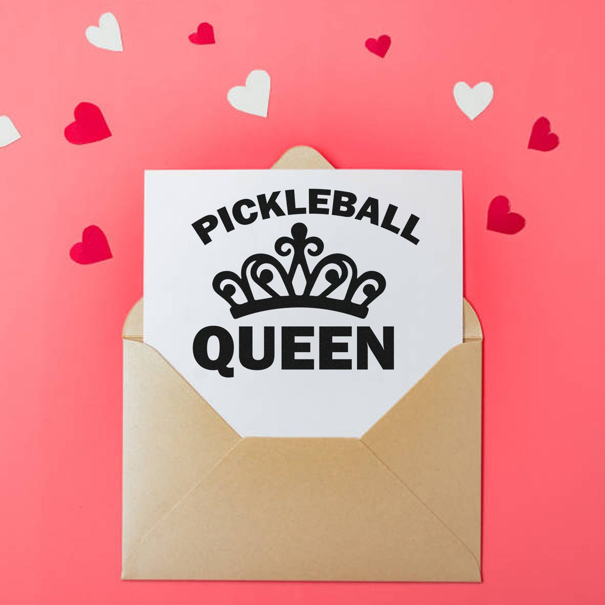 Pink background with heart confetti and a beige envelope holding a white custom stamp seal reading Pickleball Queen in black.
