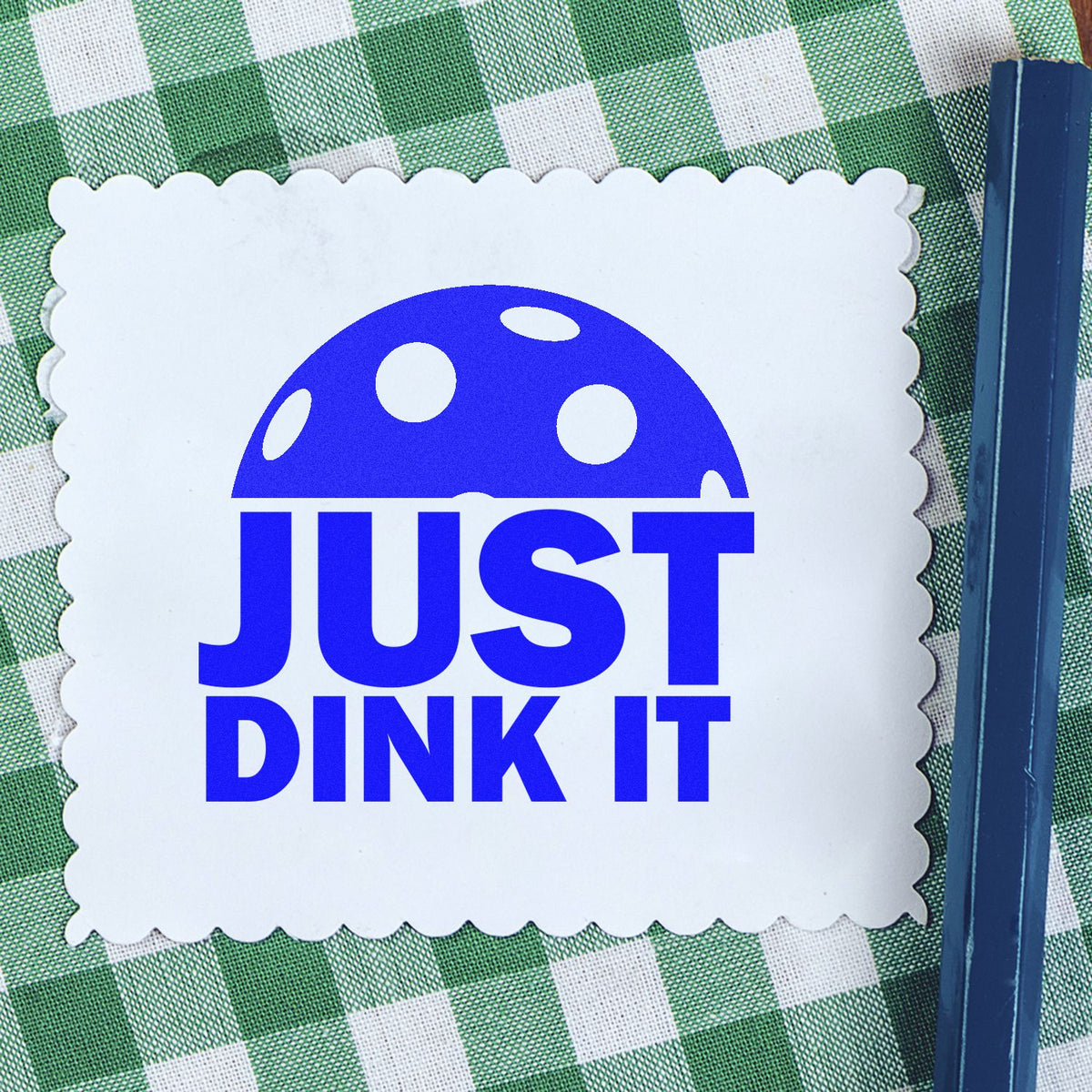Blue JUST DINK IT stamp seal on a white scalloped card over green gingham fabric, with a dark blue handle on the right.