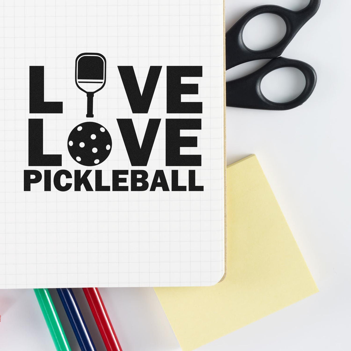 Black LOVE LOVE PICKLEBALL stamp and seal design with paddle and ball icons on white grid paper, plus scissors and a sticky note.