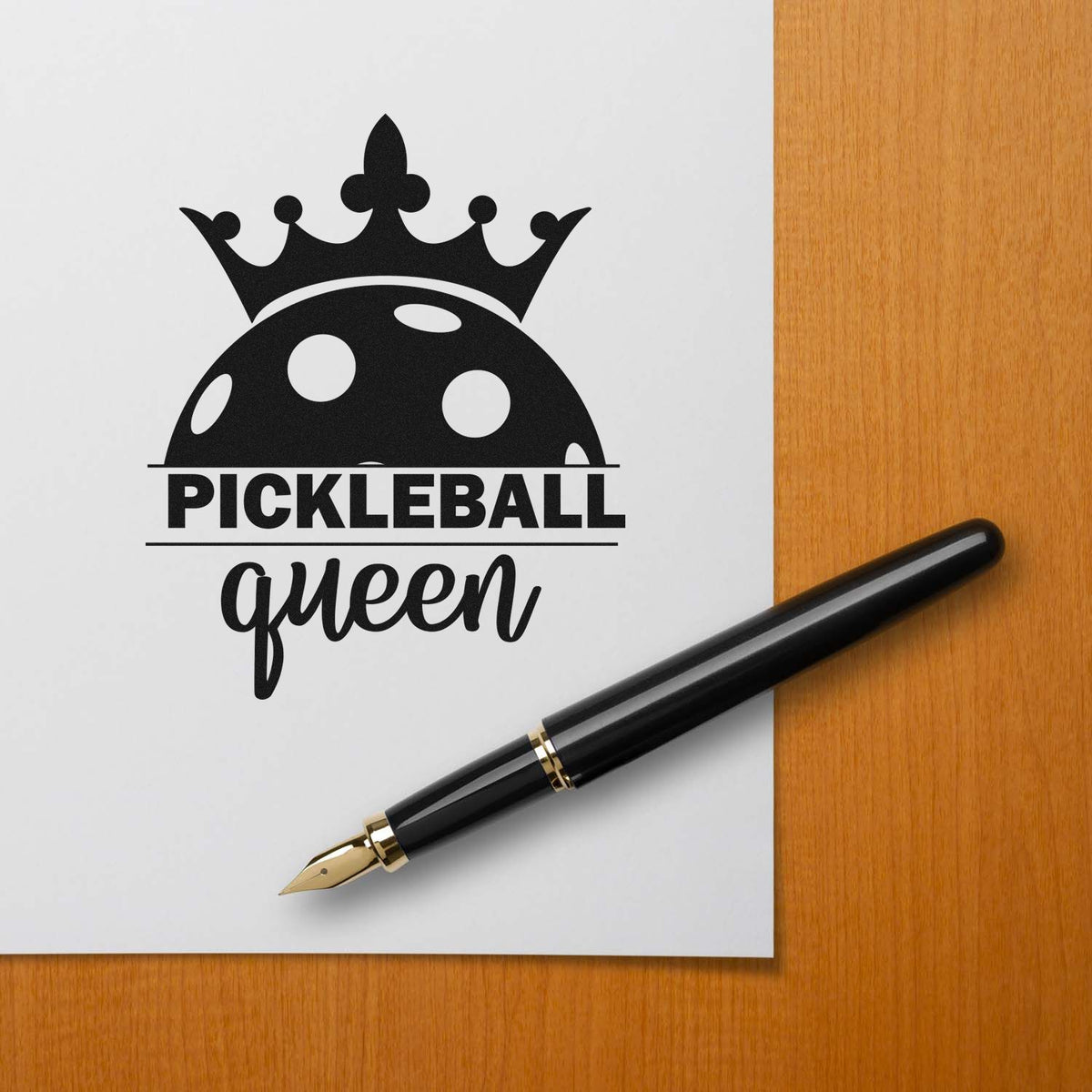 Black Pickleball Queen stamp seal with crown and paddle ball graphic on white paper beside a black fountain pen.