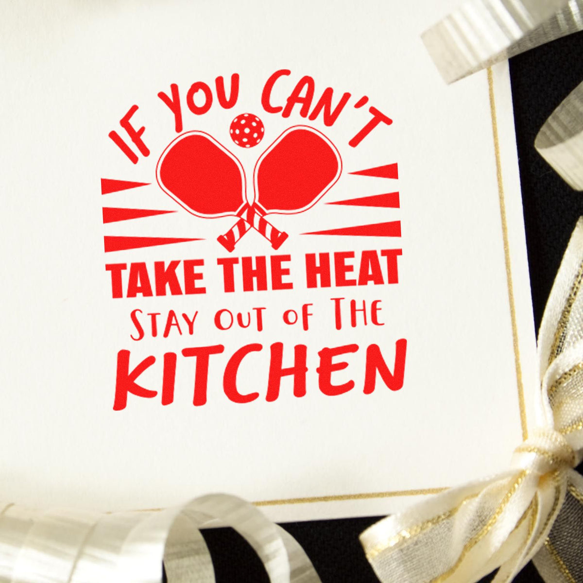 Red stamp and seal with paddles, saying If you cant take the heat, stay out of the kitchen, on a white card with ribbon.