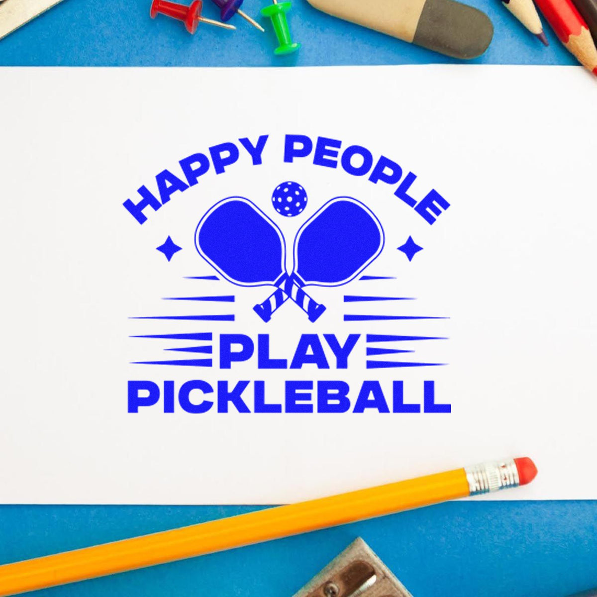 Blue Happy People Play Pickleball stamp with paddle and ball logo on white paper, framed by colorful pencils.