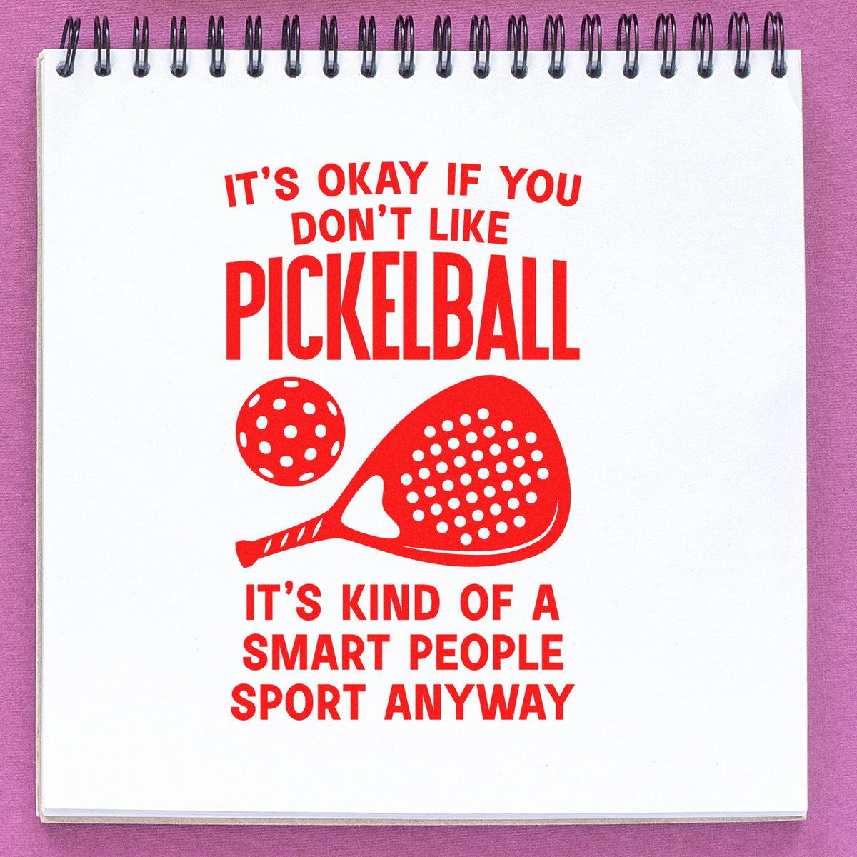 Red pickleball stamp and seal design with paddle and ball, bold text on white spiral notebook page against pink background