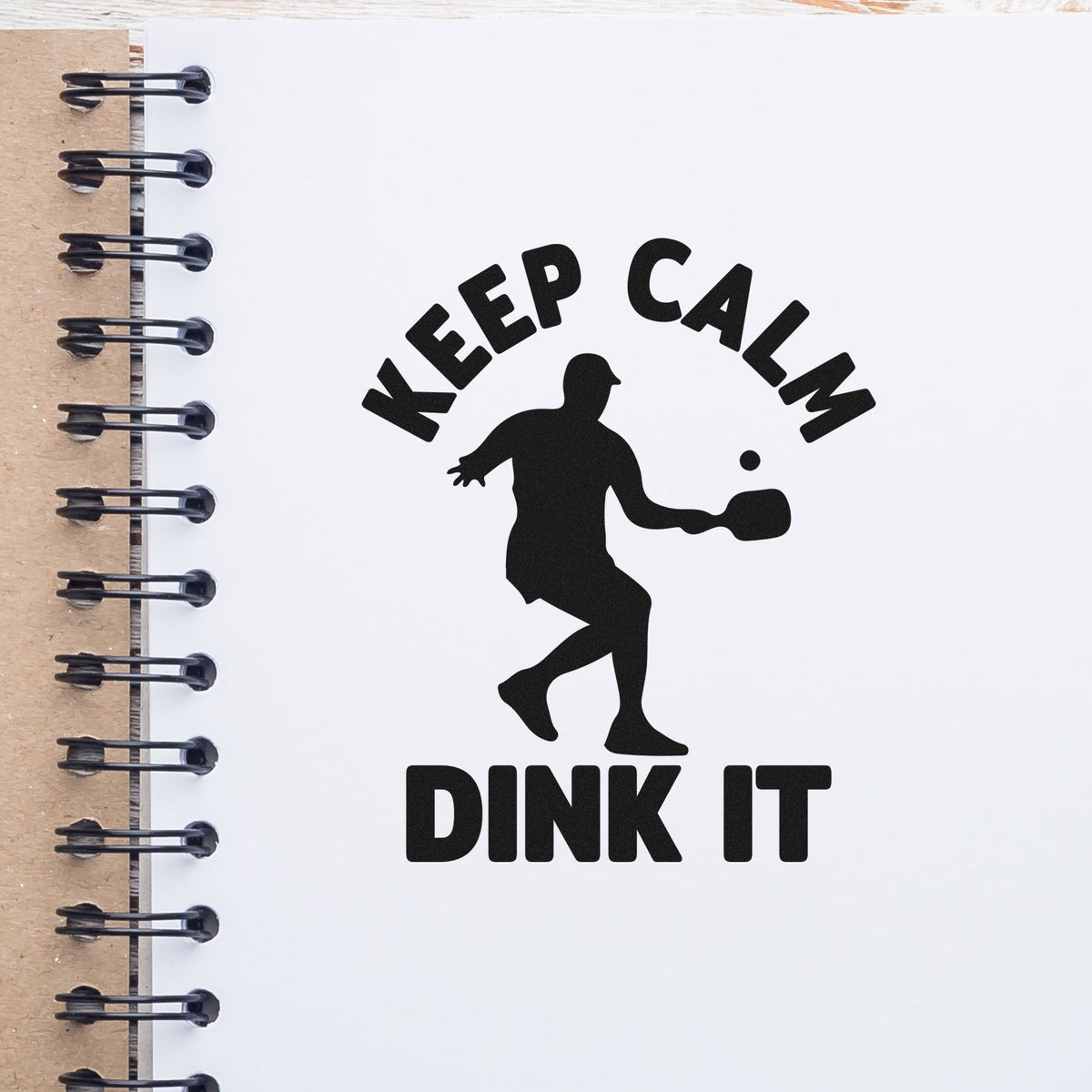 Black KEEP CALM DINK IT stamp seal with pickleball player silhouette on a white spiral notebook page.
