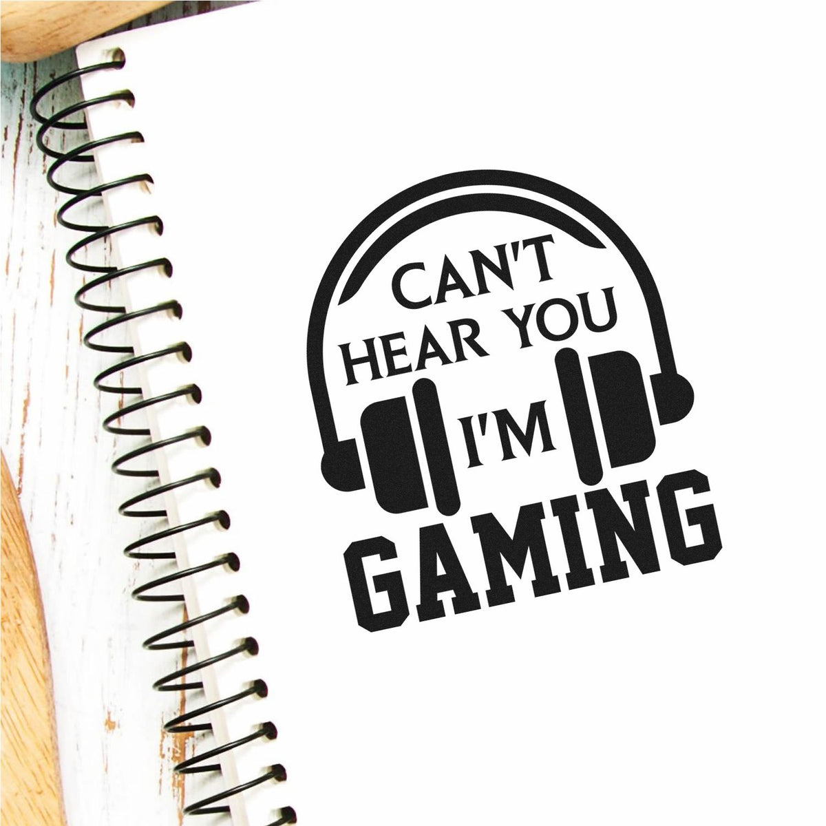 Black gaming stamp seal with headphones and the text Cant hear you, Im gaming on a white notebook.