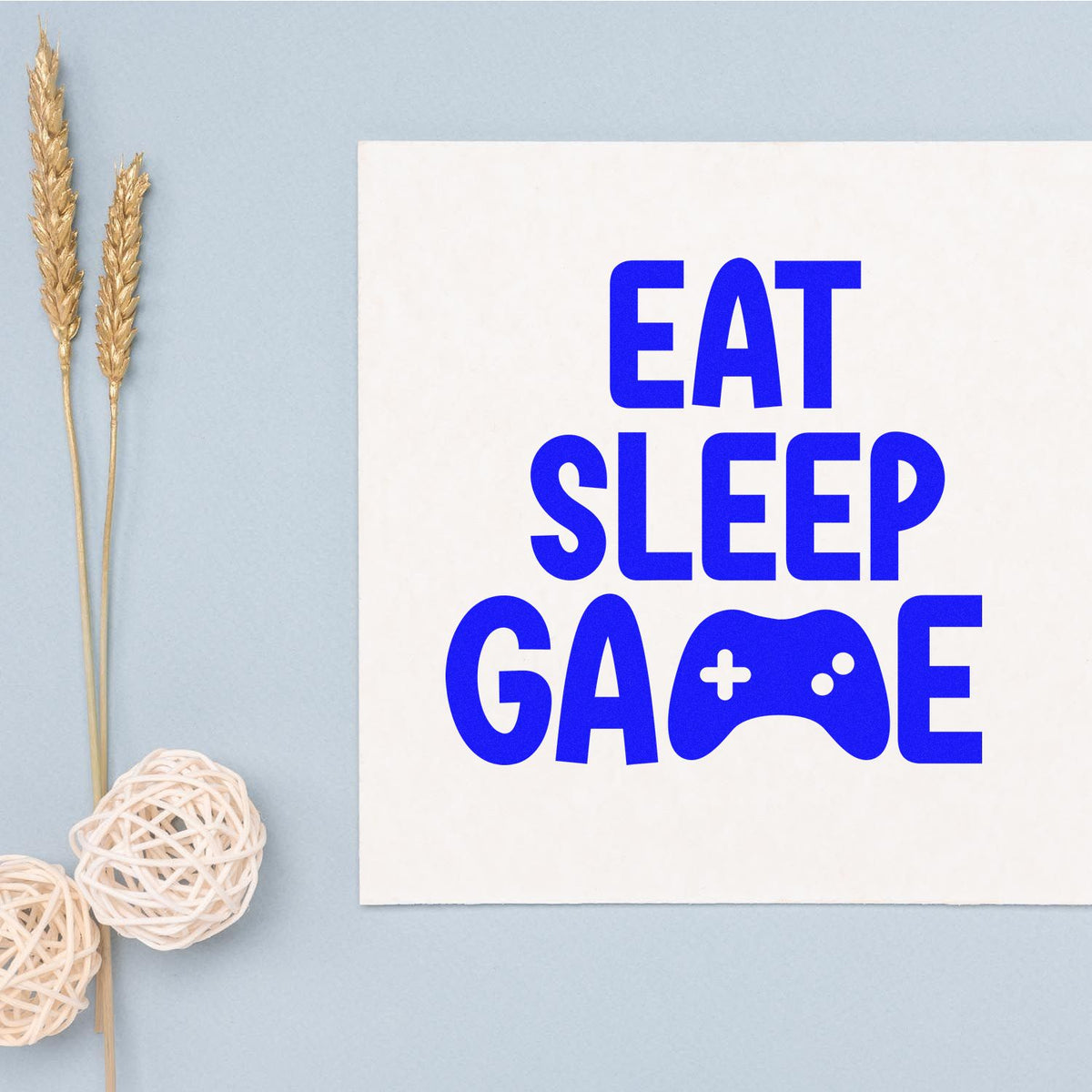 Blue EAT SLEEP GAME stamp and seal design with game controller icon on a white card, styled on a light blue background.