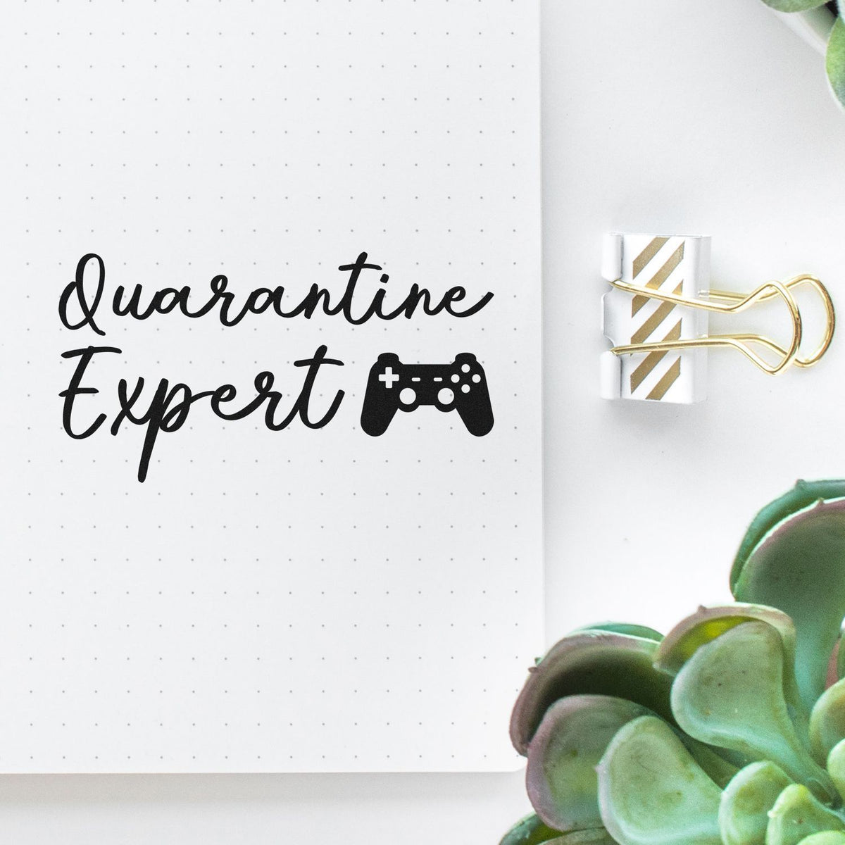 Black Quarantine Expert stamp and seal with game controller icon on white dotted paper, clipped with a gold striped binder clip