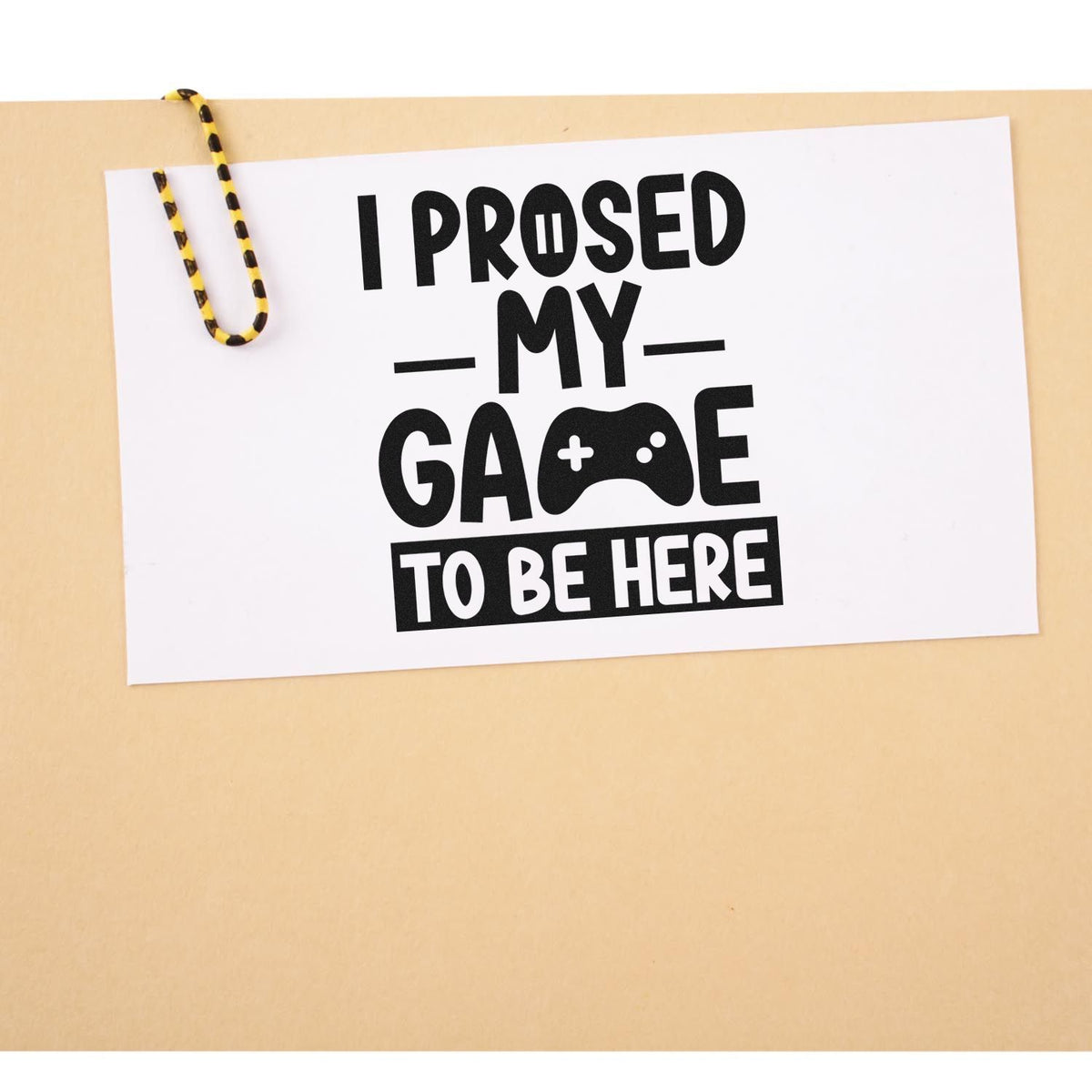 Black stamp-style quote on white card with yellow-and-black cord clip, on beige background, reading I Proused My Game To Be Here.