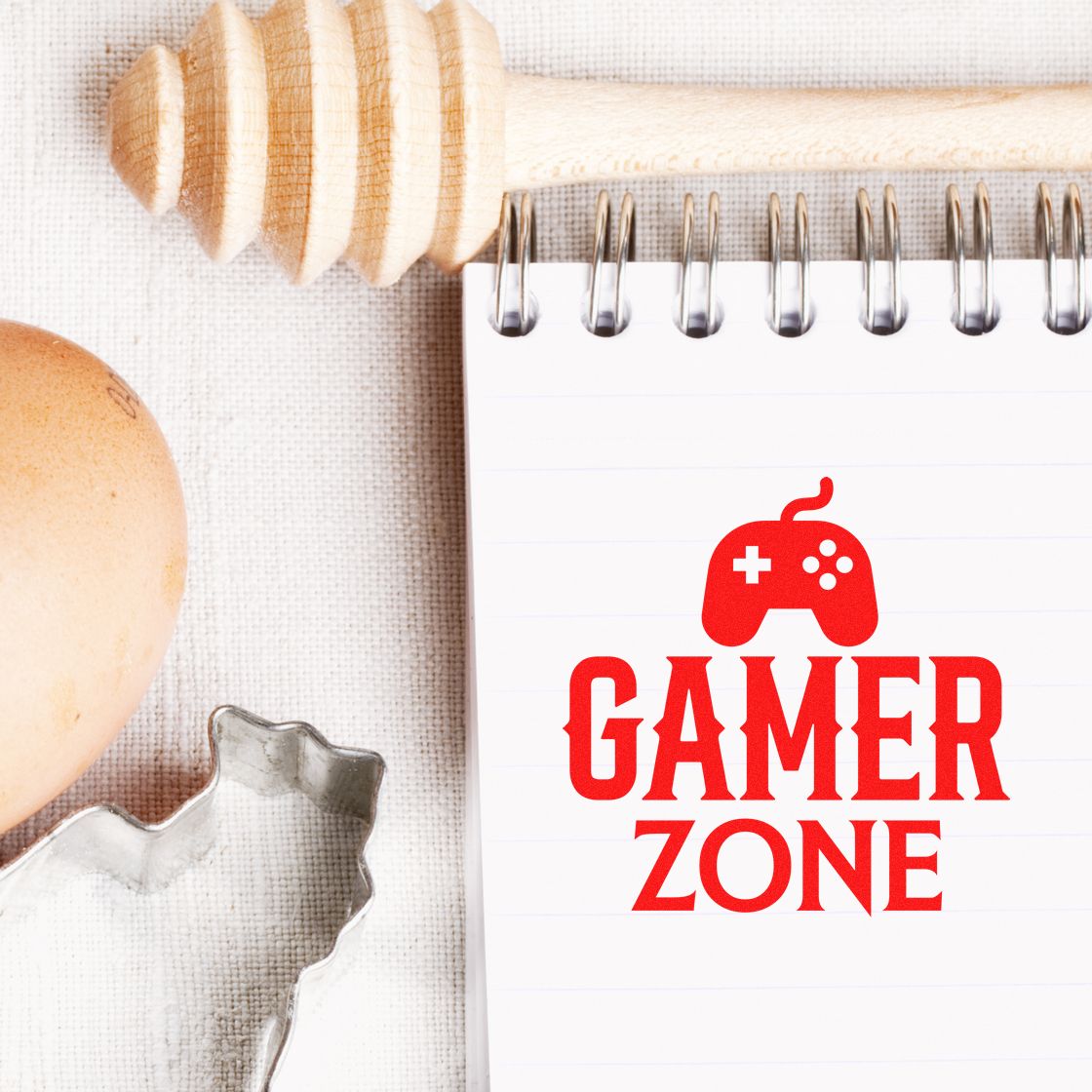 Red Gamer Zone stamp and seal design on white spiral notebook, with wooden stamp handle and metal seal cutter.