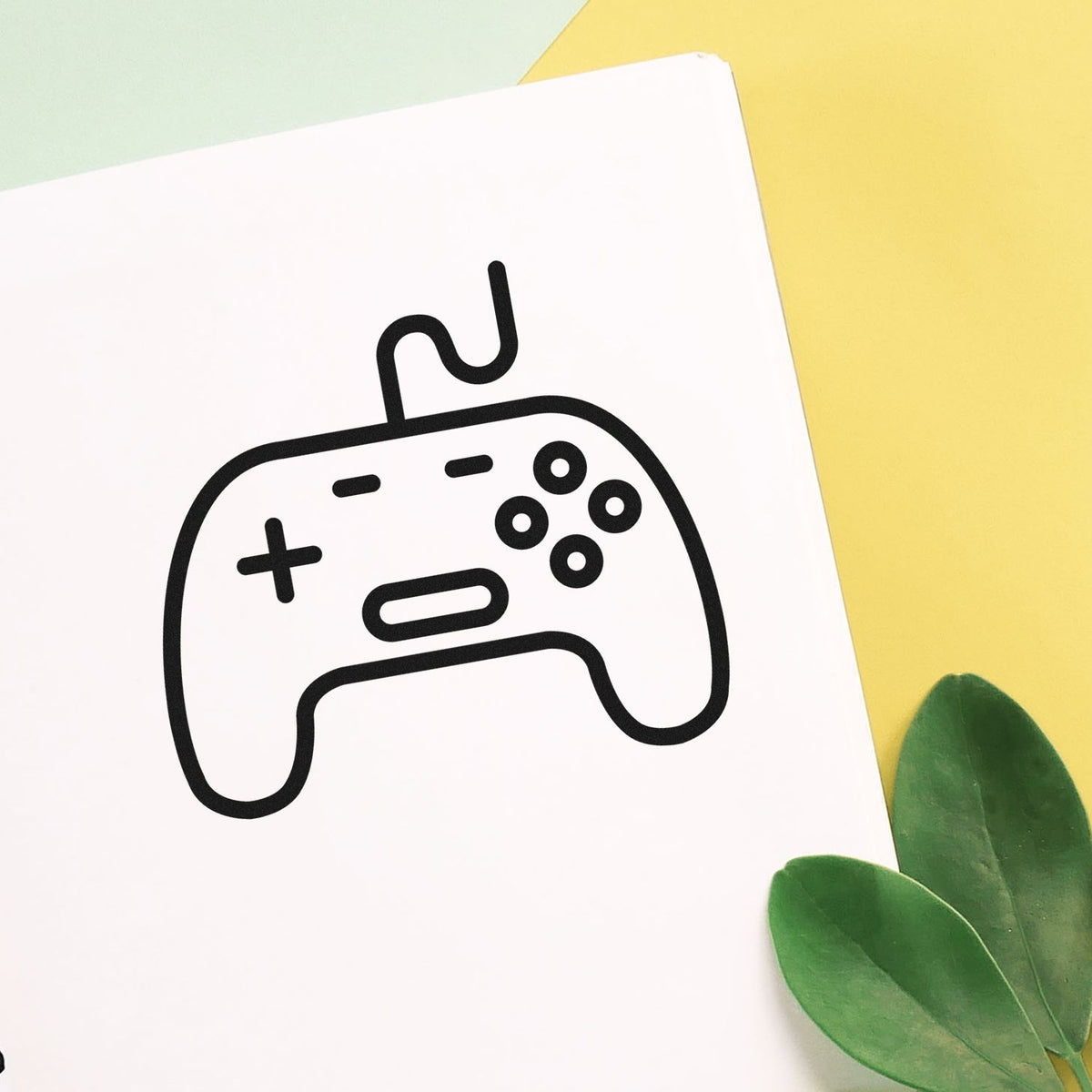 Black controller stamp and seal design on white card with pastel yellow background and green leaves.