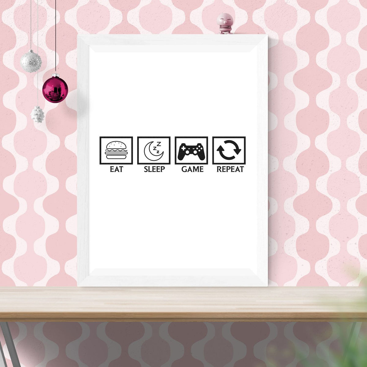 White framed stamp art with black EAT SLEEP GAME REPEAT seal icons on a pink patterned wall.