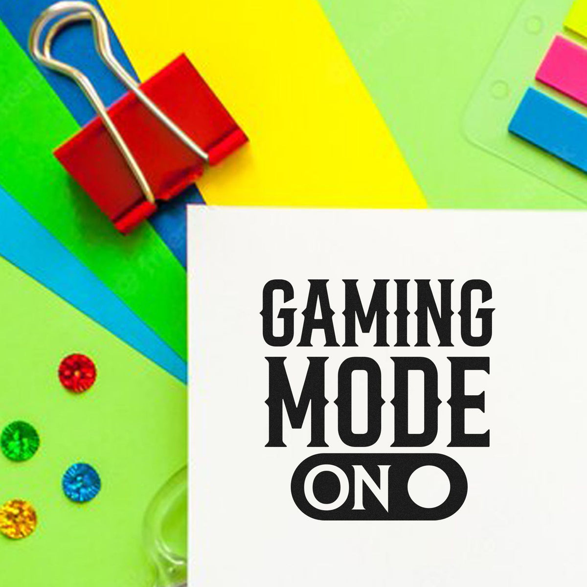 Colorful stamp and seal products with red binder clip and white card reading GAMING MODE ON on bright green, yellow, and blue background.