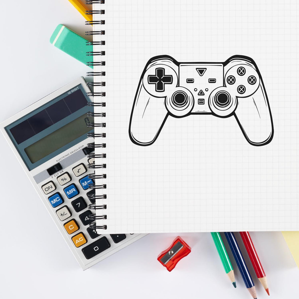 Black game controller stamp seal on graph paper notebook, with calculator, colored pencils, and eraser on white desk.