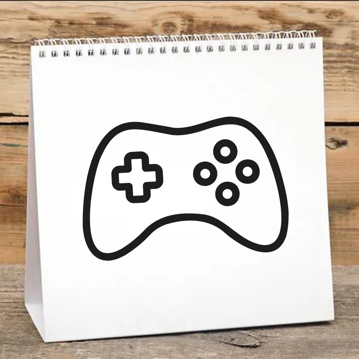 Black game controller stamp and seal on white spiral-bound notepad, on rustic wood table.