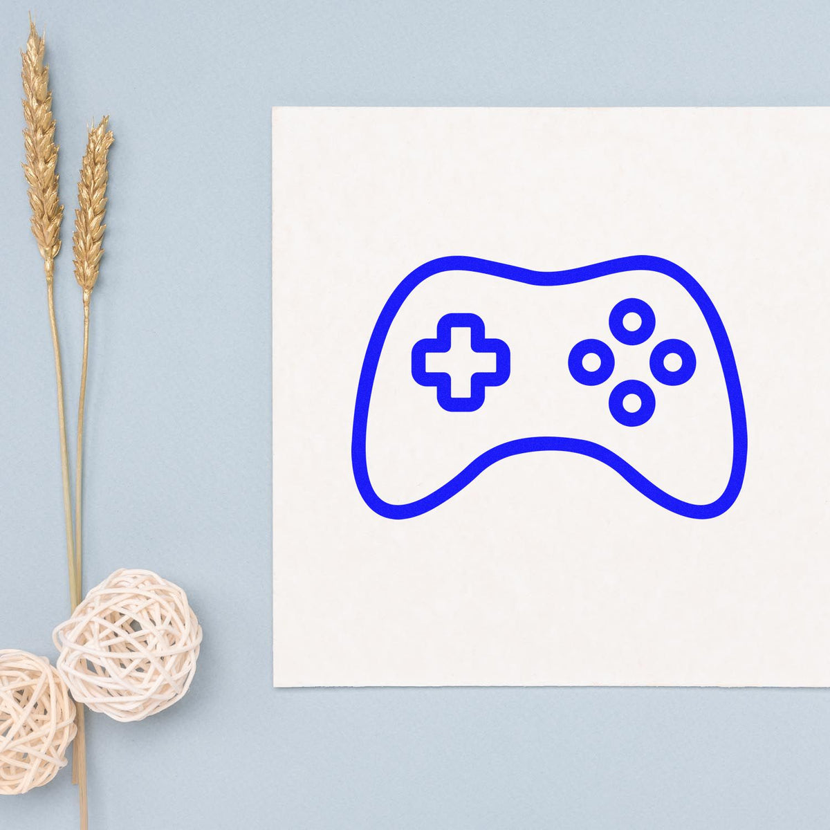 Blue game controller stamp seal design with cross and buttons on a white card, on a light blue background.
