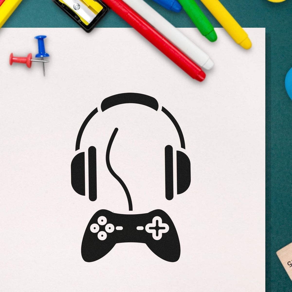 Custom stamp and seal design: black gaming headset and controller on white paper, surrounded by colorful pens and push pins.