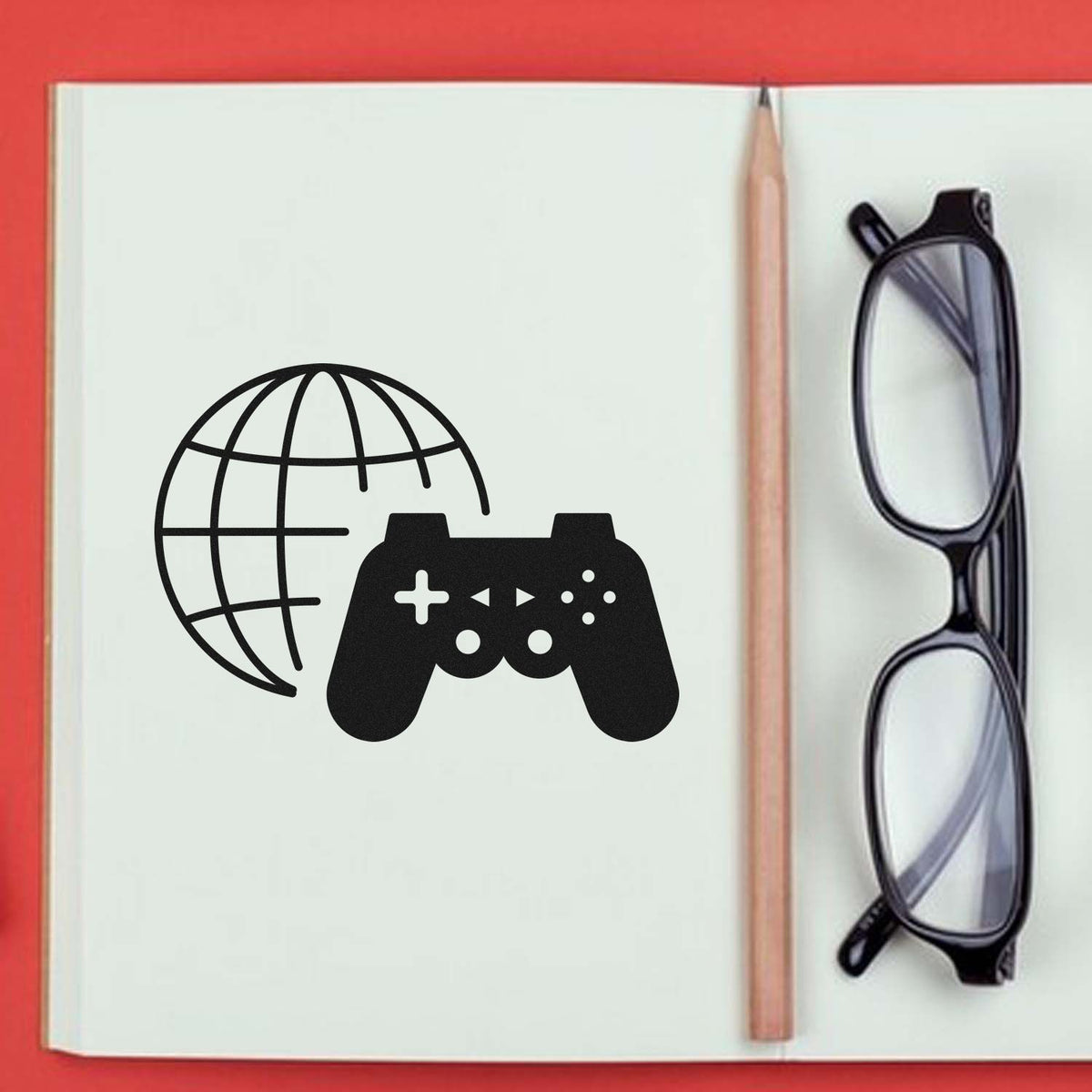 Black stamp and seal logo with globe and game controller on an open notebook, beside a pencil and black glasses.