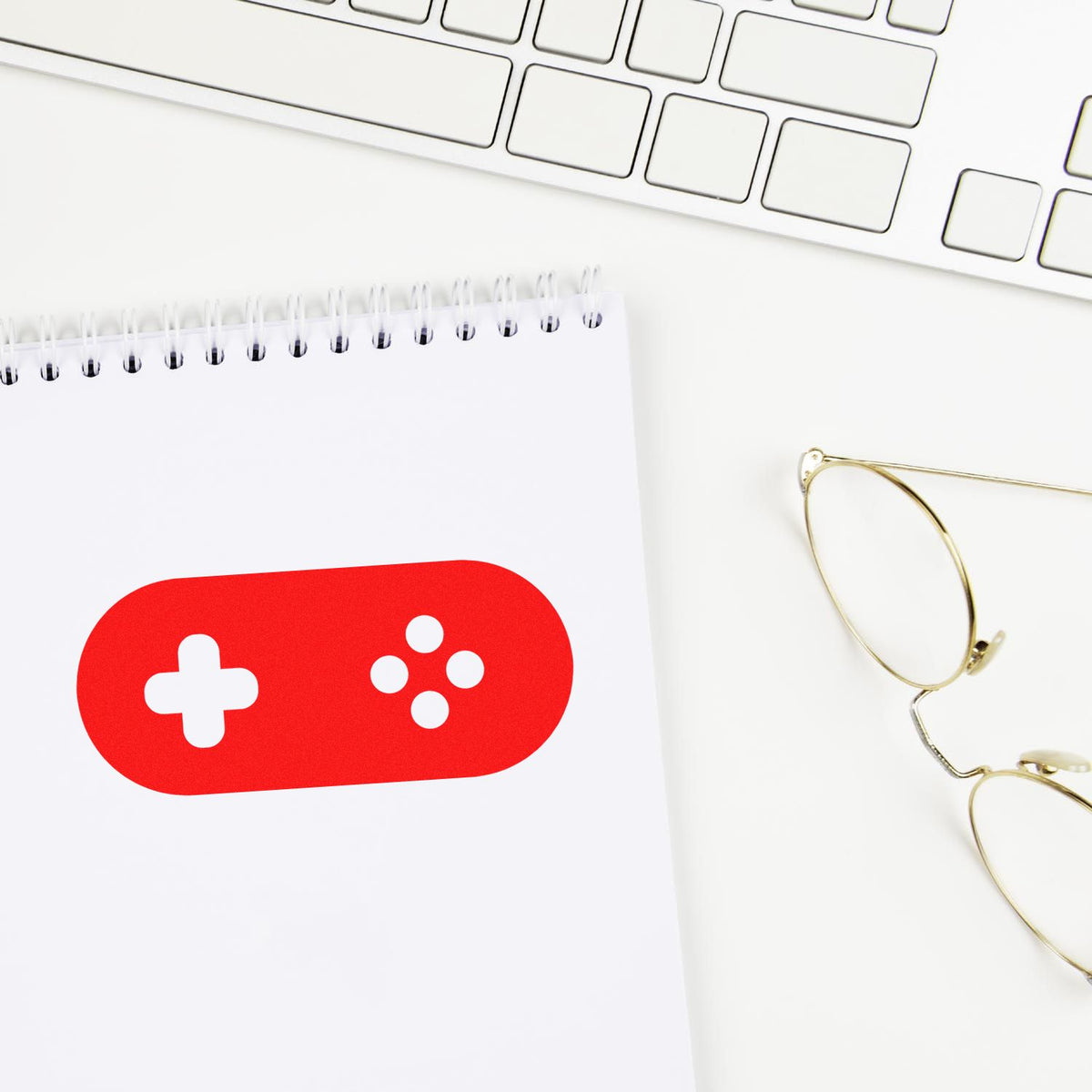 Red stamp-and-seal design with a white plus and four dots on a notebook, beside gold glasses and a white keyboard.