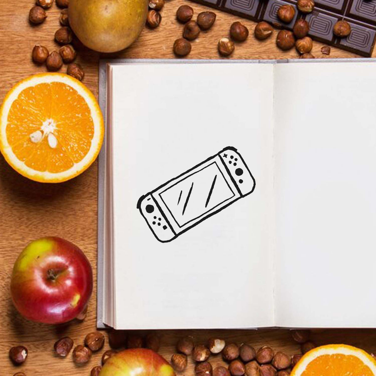 Black stamp and seal design on open white notebook, with oranges, apples, and coffee beans on a wooden table.