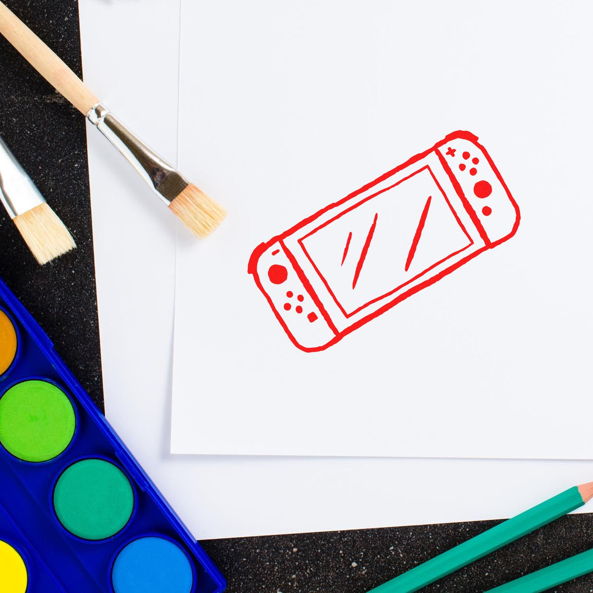Red rubber stamp seal on white paper, with paintbrushes, watercolor palette, and teal pencils.