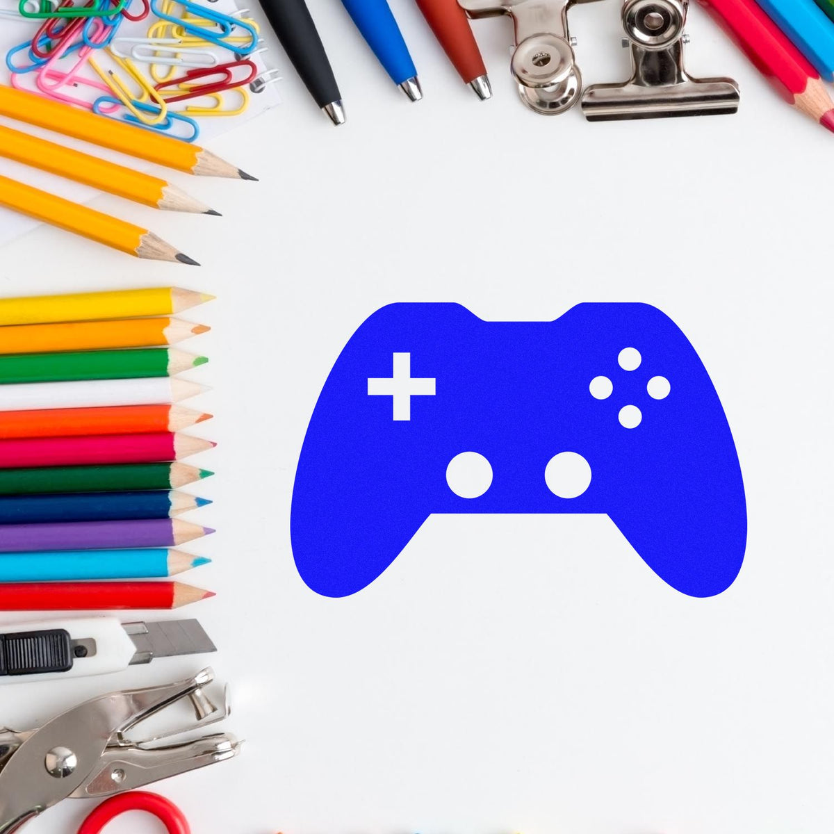 Blue game controller stamp and seal surrounded by colorful pencils, paper clips, pens, and metal office tools on white background