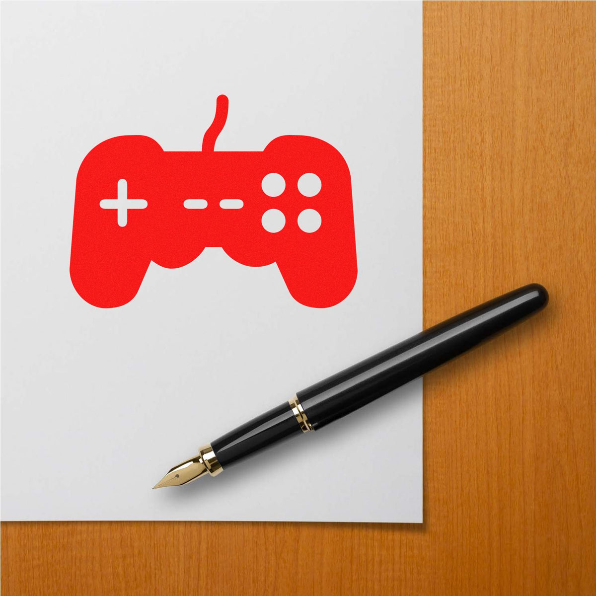 Red game controller stamp and seal on white paper, with a black fountain pen on a wood desk.