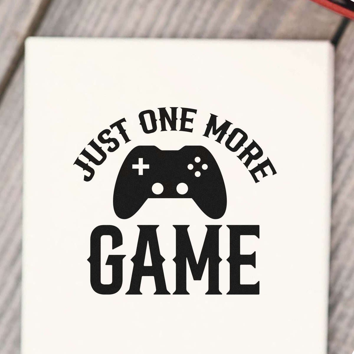 Black Just One More Game stamp seal with a game controller icon on a white background