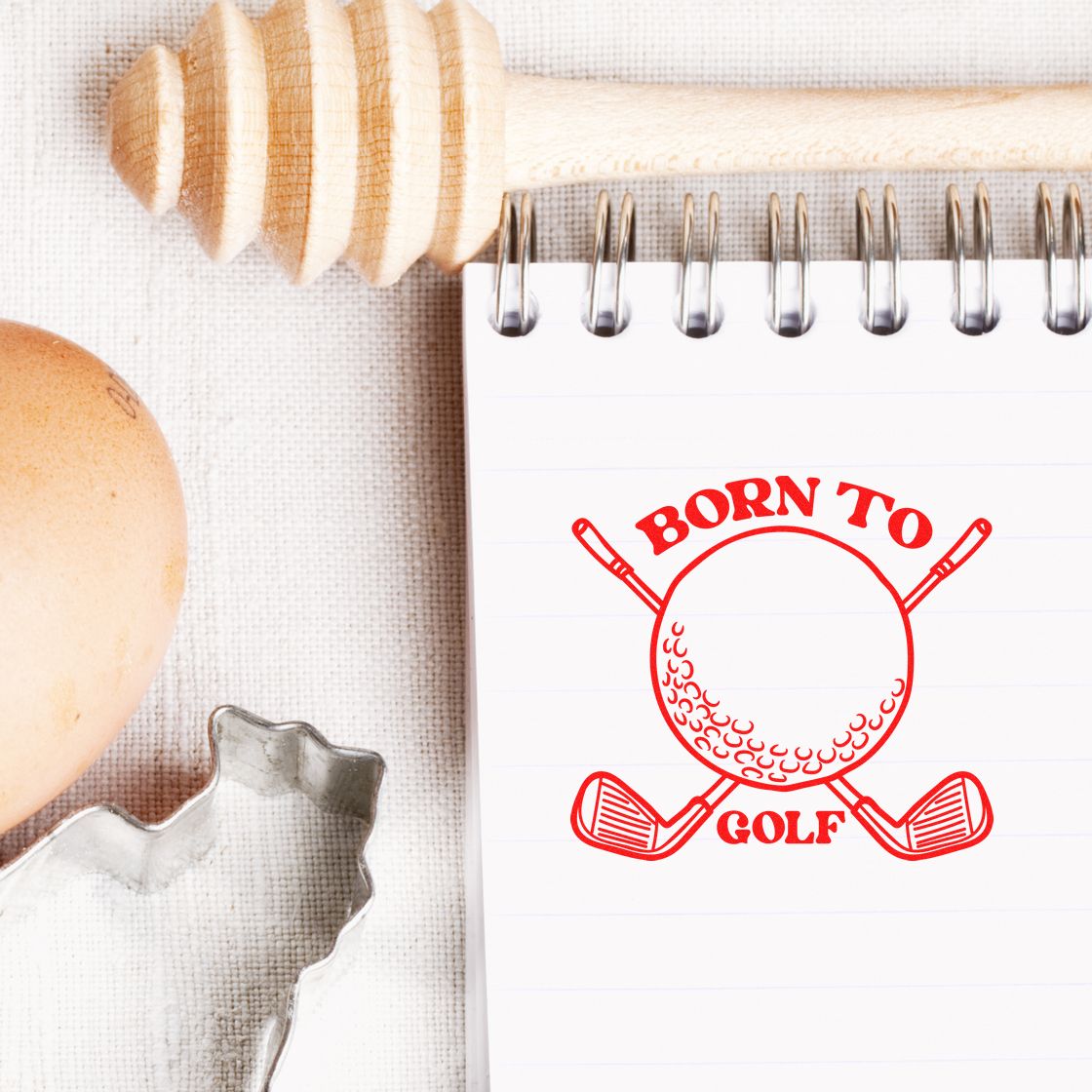 Red Born to Golf stamp seal with golf ball and crossed clubs on a white spiral notebook