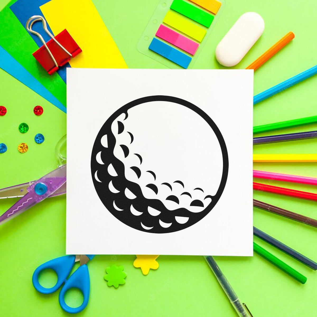 Black circular stamp seal design on white card, surrounded by colorful stationery on a green background.