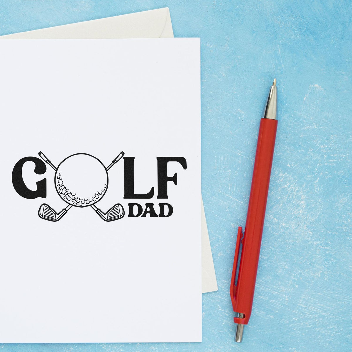 Golf dad stamp design on white card, black lettering with golf ball and clubs, beside a red pen on a blue background.