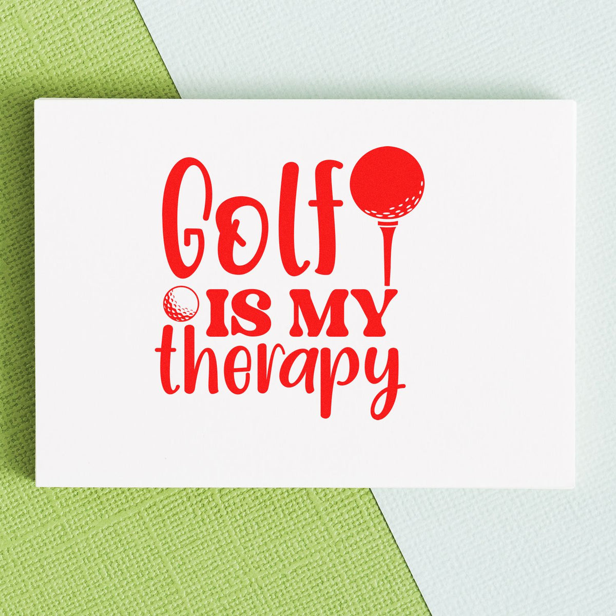 Red golf stamp and seal reading Golf is my therapy with golf ball tee on white card, on green textured background.