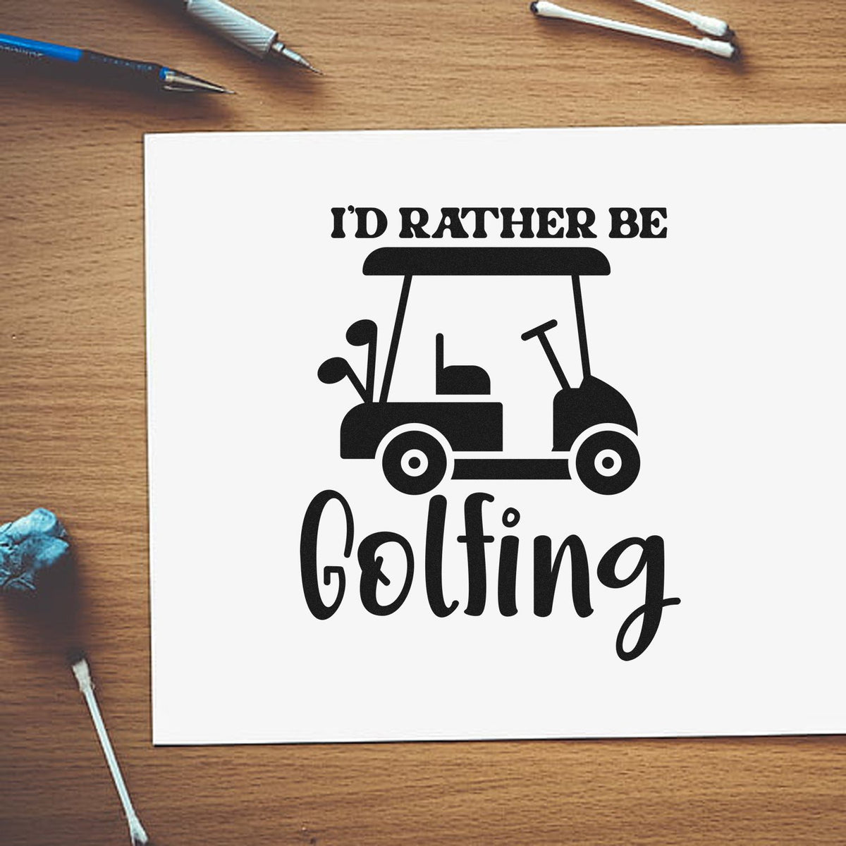 Black rubber stamp/seal design reading 'I'd rather be golfing' with golf cart on white paper, on a wood desk.