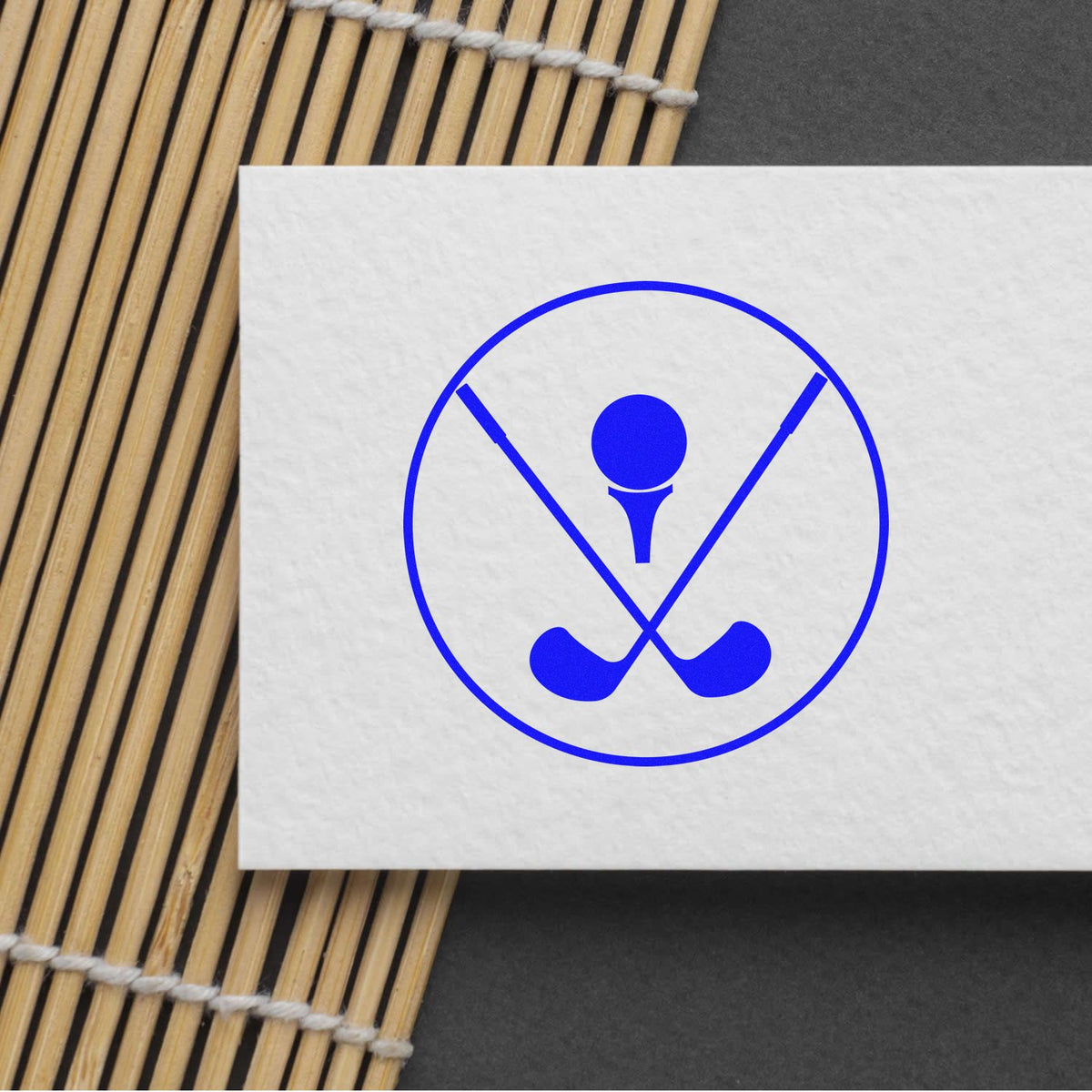 Blue golf stamp seal logo with crossed clubs inside a circle on white paper, set on a bamboo mat.