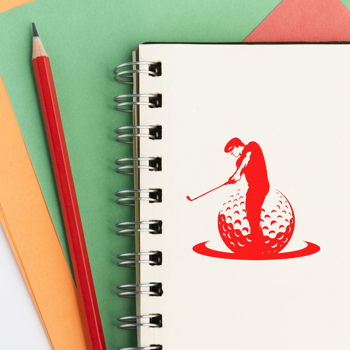 Red golf stamp seal on a white spiral notebook beside a red pencil, set against green and orange paper.