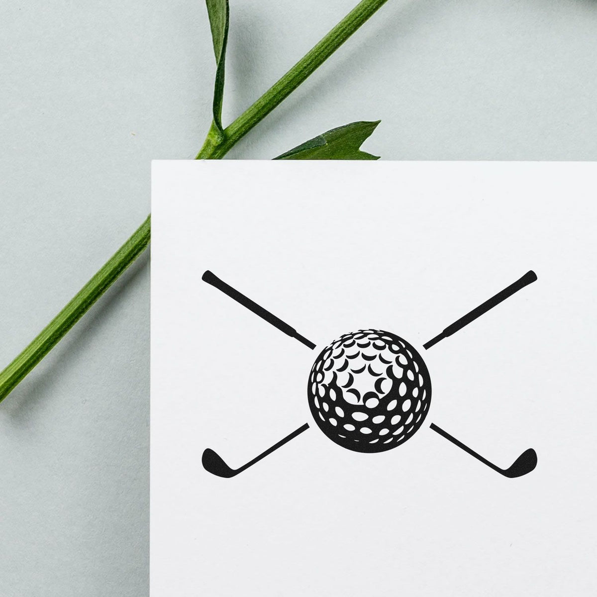 Black golf ball and crossed clubs stamp/seal on white card, with green stems in background
