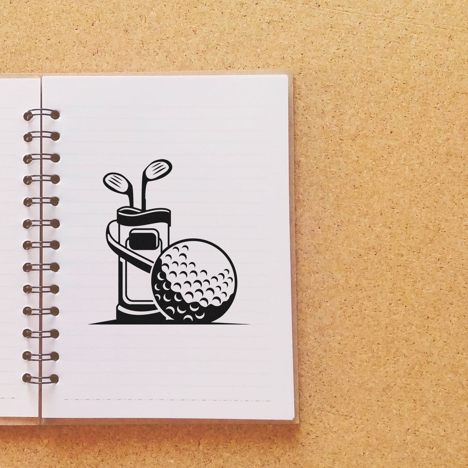 Black golf bag and ball stamp seal on white spiral notebook over tan cork background.