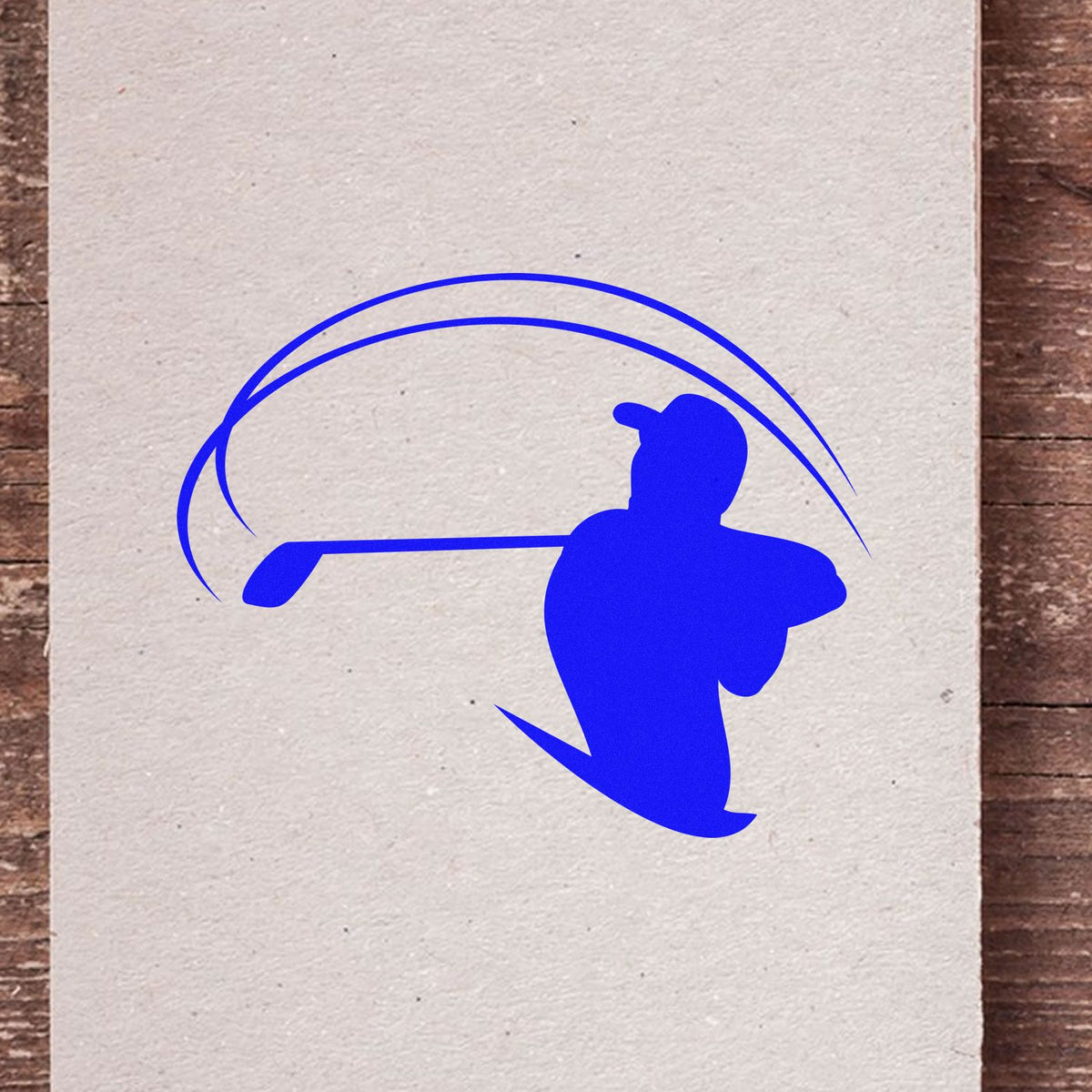 Blue golf stamp and seal design with golfer silhouette and swing arcs on white paper over a wood background.