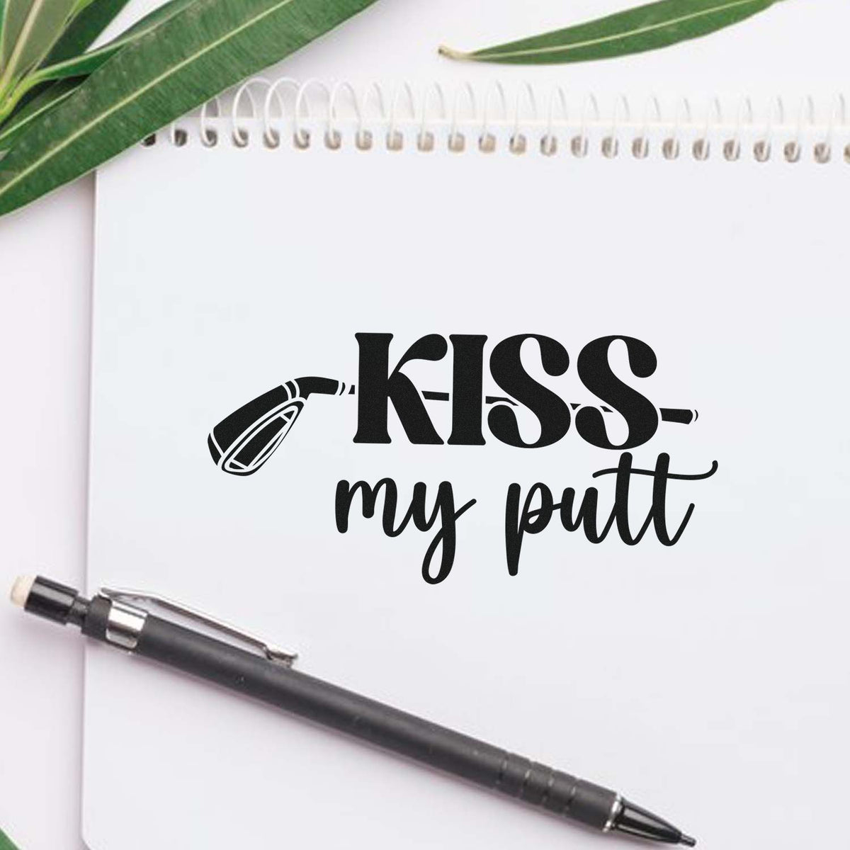 Black custom stamp-and-seal design reading KISS my butt on a white notebook, with lipstick graphic, pen, and green leaves.