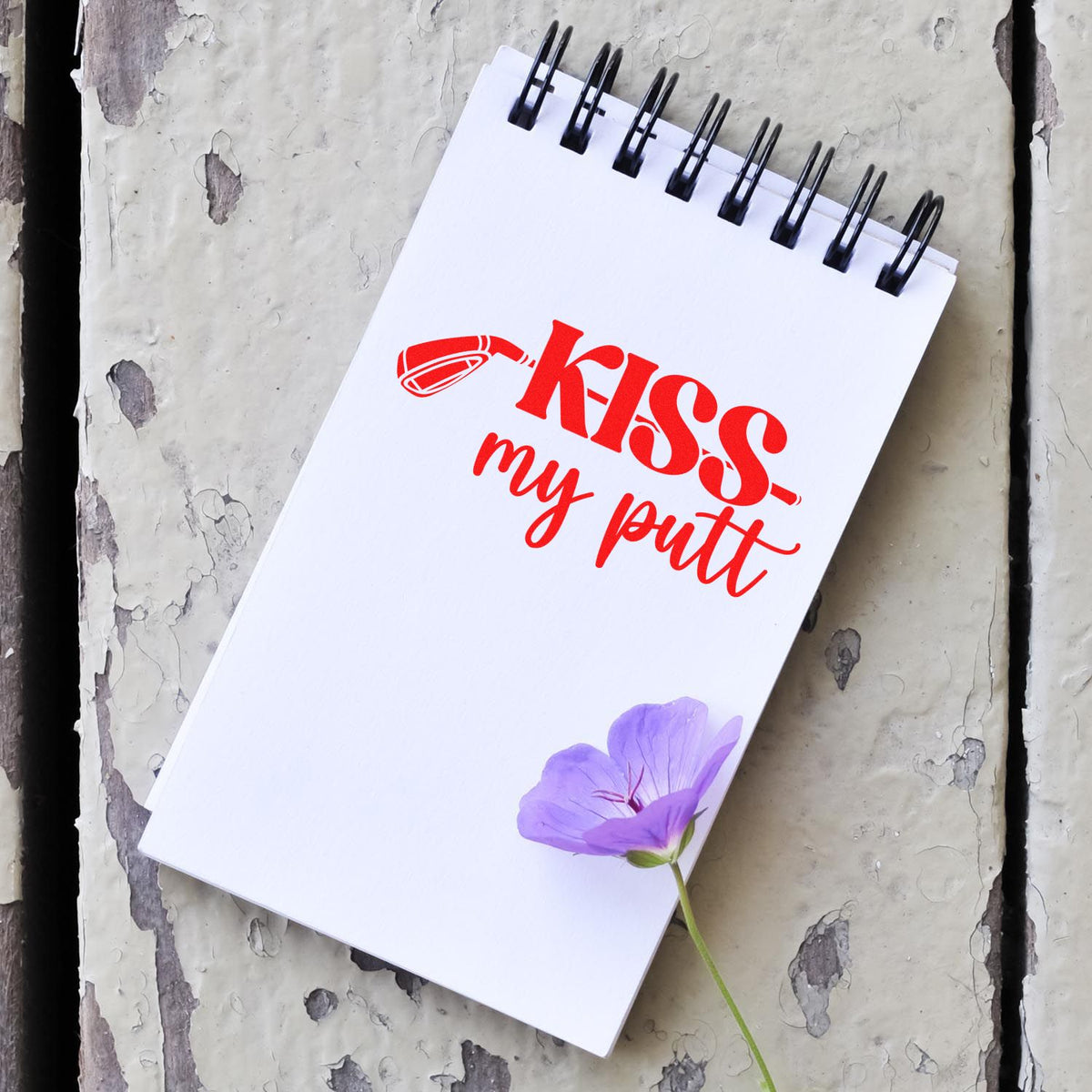 Custom stamp and seal notebook with red kiss my putt print, purple flower accent, on weathered white wood.