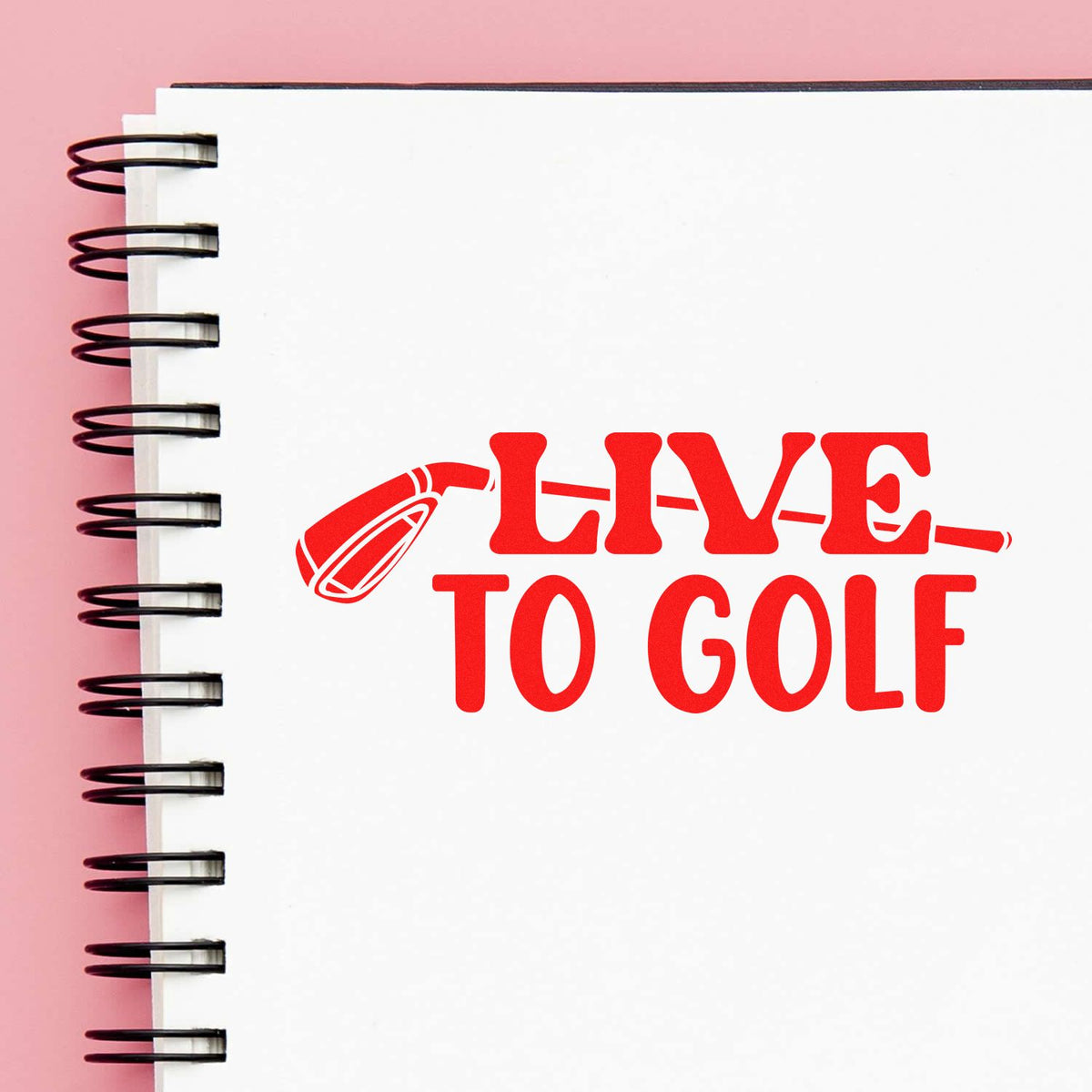 Red LIVE TO GOLF stamp seal with golf club icon on a white spiral notebook over a pink background.