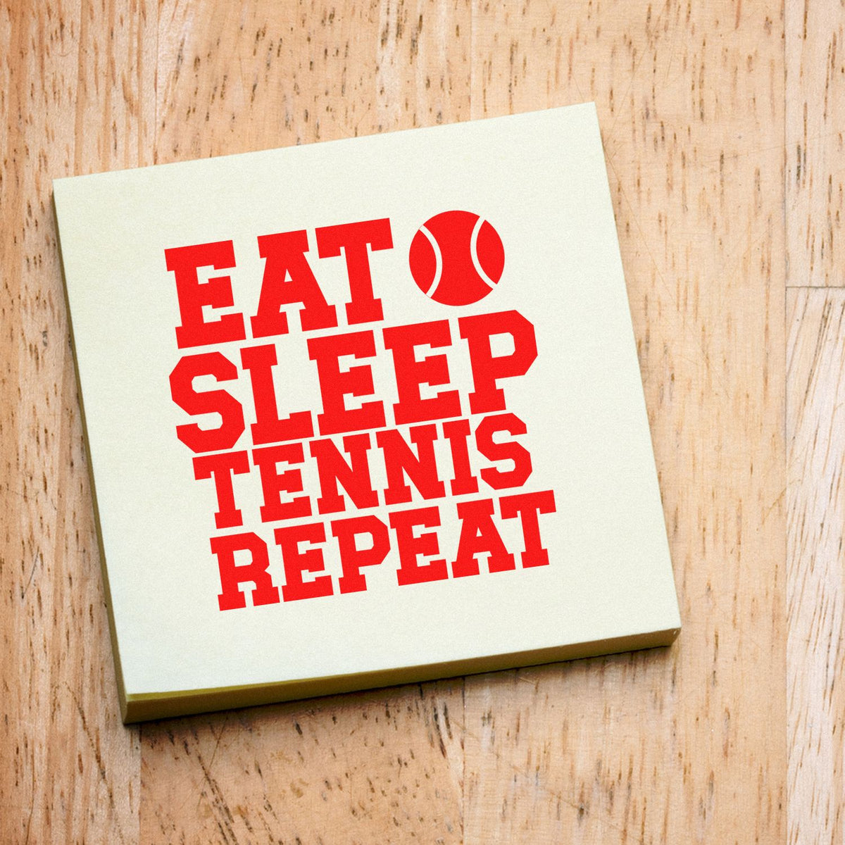 Cream square rubber stamp featuring bold red Eat Sleep Tennis Repeat text and a tennis ball icon on wood.