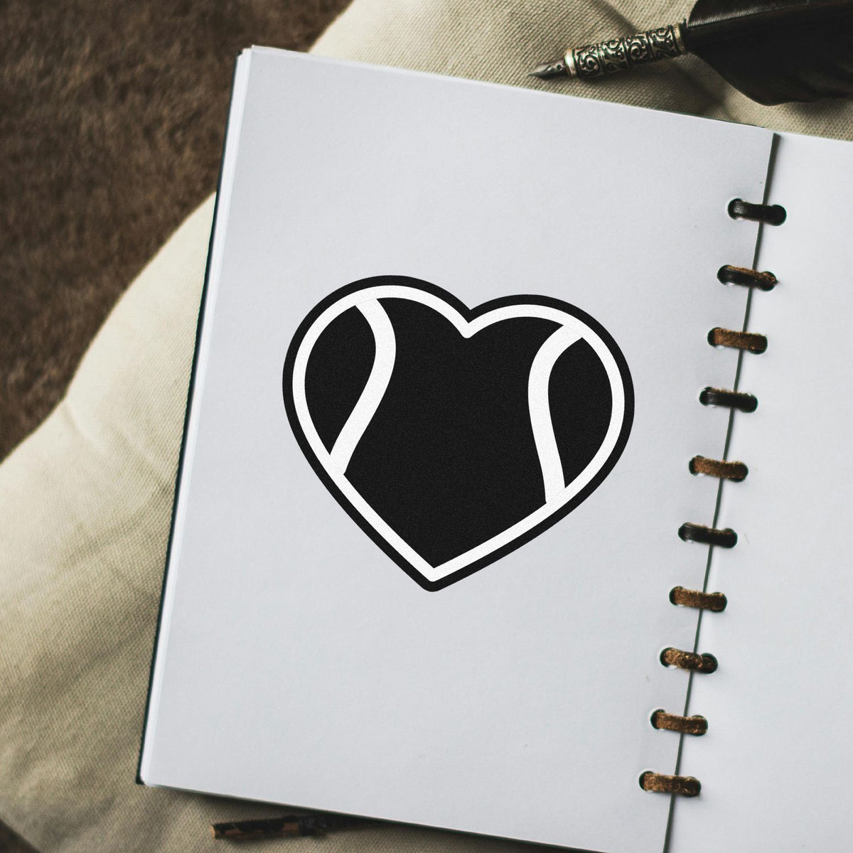 Black heart seal stamp on white spiral-bound notebook with brown binding and ornate pen nib