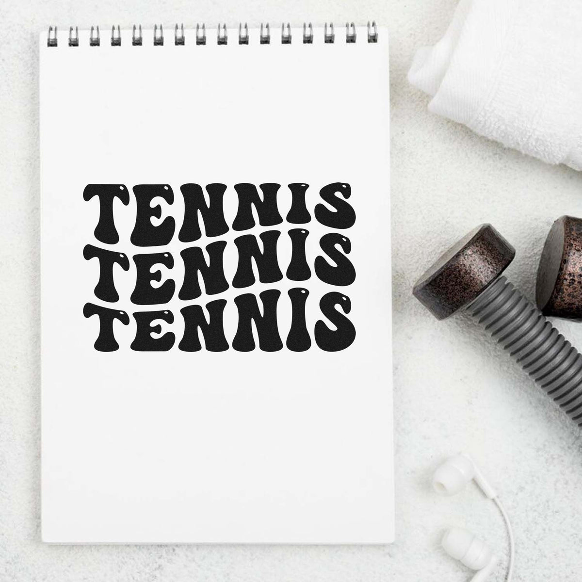 White spiral notebook with bold black TENNIS stamp design, beside rubber stamp and seal tools on a white background.