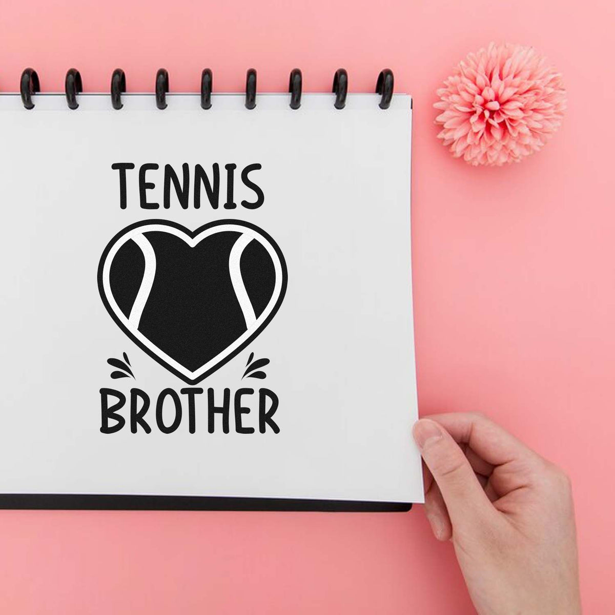 Custom tennis brother stamp and seal design in black on a white spiral notebook, with heart graphic on a pink background.