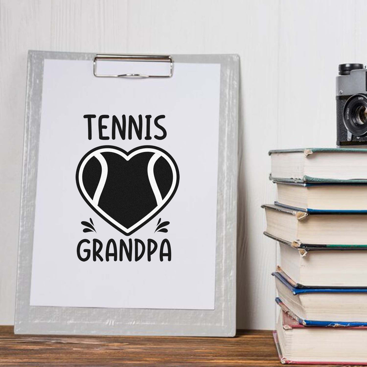 Black Tennis Grandpa stamp and seal design with heart tennis ball on white clipboard, gray frame, and stacked books.
