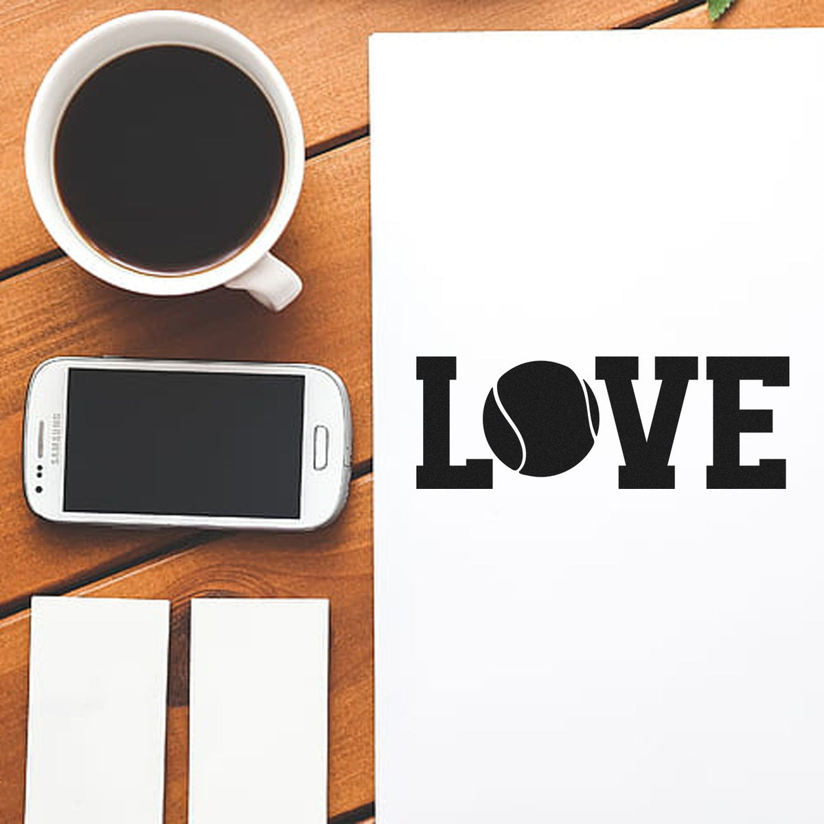 Black LOVE stamp and seal products on white paper beside a smartphone, coffee cup, and blank cards on a wooden desk.