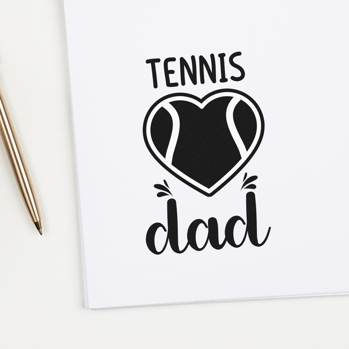 Black tennis dad stamp seal with heart-shaped tennis ball graphic on white paper, gold pen beside it.