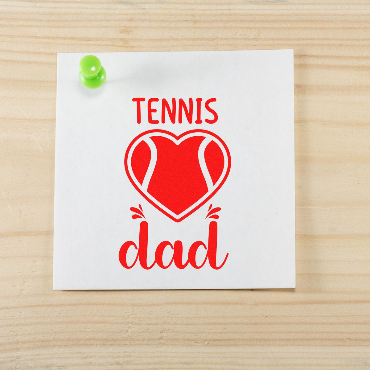 Red tennis dad stamp with heart-shaped tennis ball design on white paper, pinned with green pushpin on wood background.